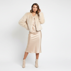 Woman wearing a beige fur coat and satin skirt on a white background