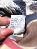 A close-up of a hand holding a white fabric care label that reads 'MACHINE WASH IN COLD WATER HANG TO DRY IRON AT MEDIUM TEMPERATURE' against a patterned textile background.
