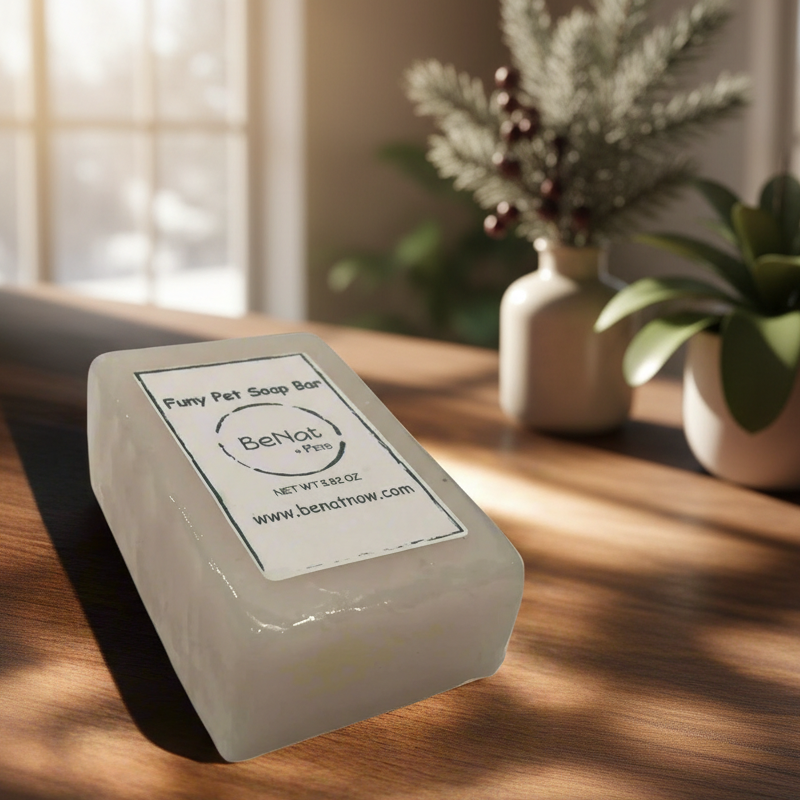 White soap bar with a label on a wooden surface, with plants and a window in the background.