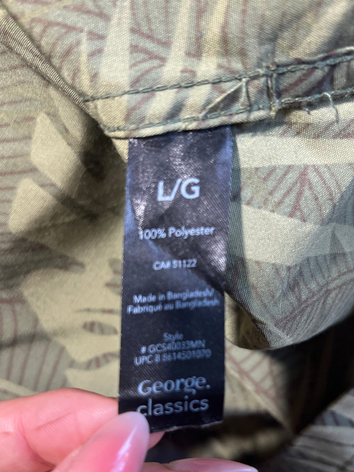 Close-up of a clothing label reading 'L/G 100% Polyester' and 'George classics' held against patterned fabric by a hand.