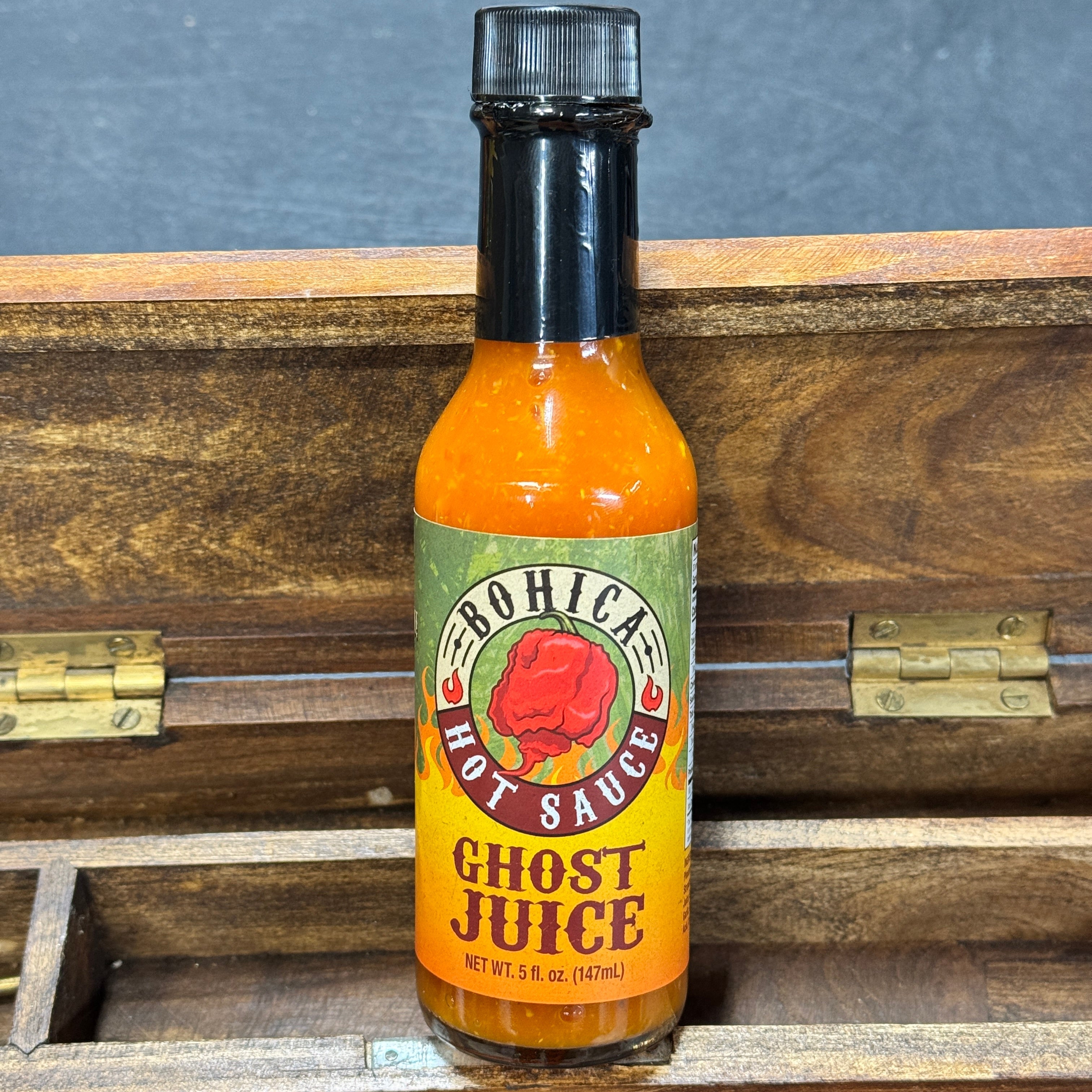 Bottle of Bohica Ghost Juice hot sauce on a wooden surface with a dark background