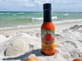 Bottle of Mohica Ghost Juice hot sauce on a sandy beach with ocean in the background