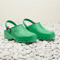 Pair of green clogs with red straps on a white background