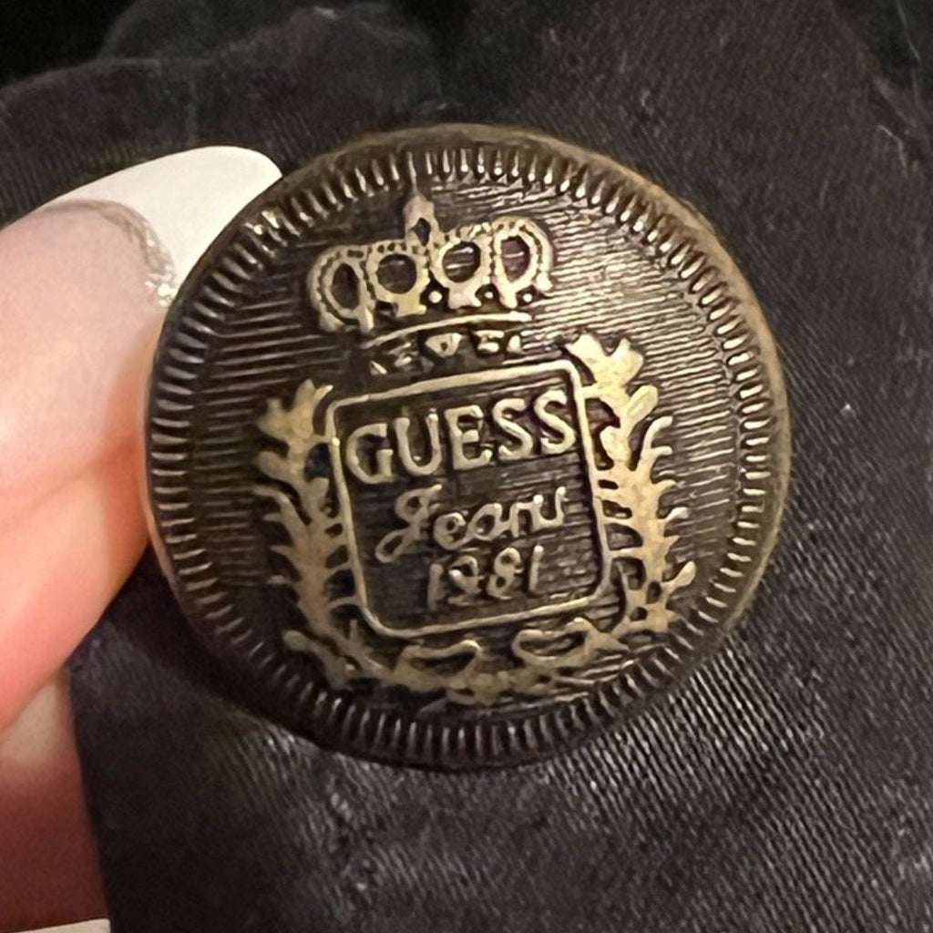 Close-up of a Guess branded button on a black fabric background