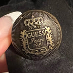 Close-up of a Guess branded button on a black fabric background