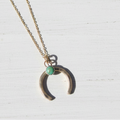 Gold necklace with a crescent moon pendant and green gemstone on a white background