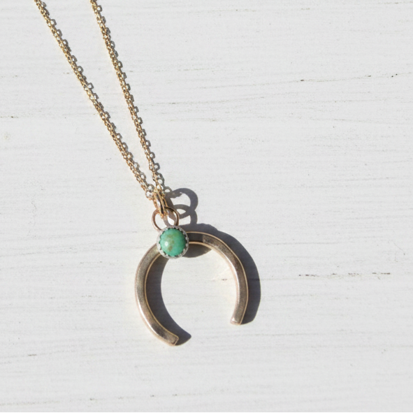 Gold necklace with a crescent moon pendant and green gemstone on a white background