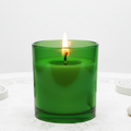 Green candle in a glass container on a white surface with a white background