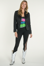 Woman in a living room wearing a black jacket, colorful top, black leggings, and white boots.