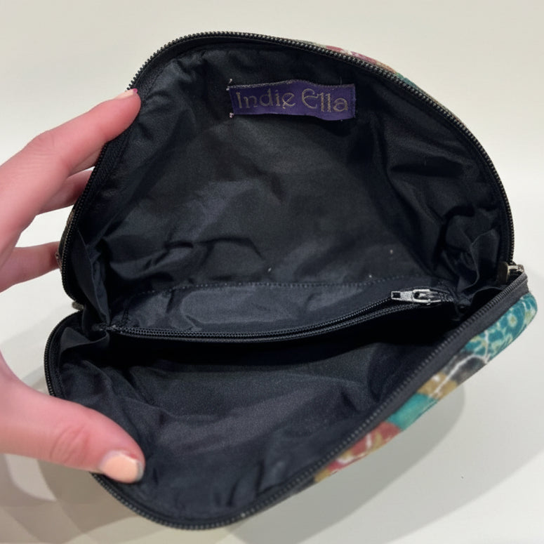 Black pouch with 'Indie Ella' label held by a hand on a textured surface
