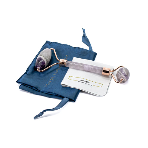 Beauty roller with purple stones on a blue satin bag and white card with brand name on a white background