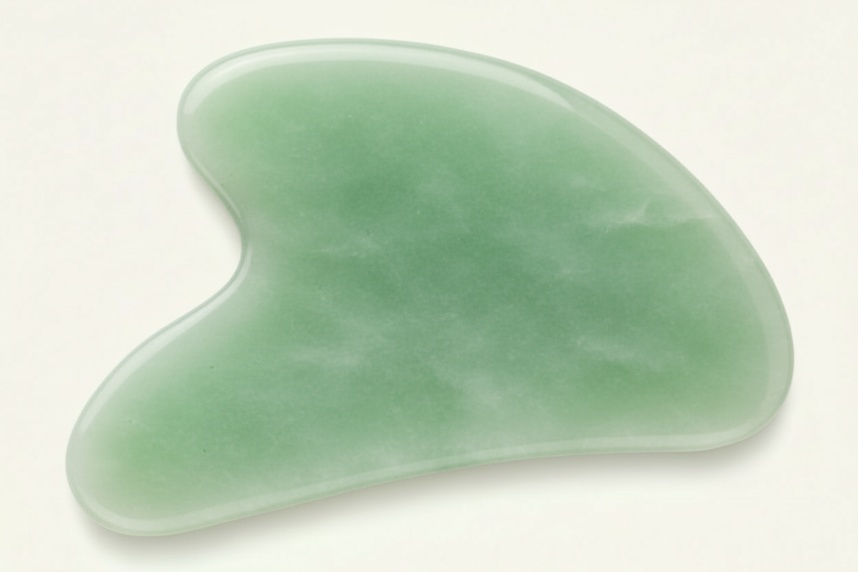 Green jade gua sha tool on a white background