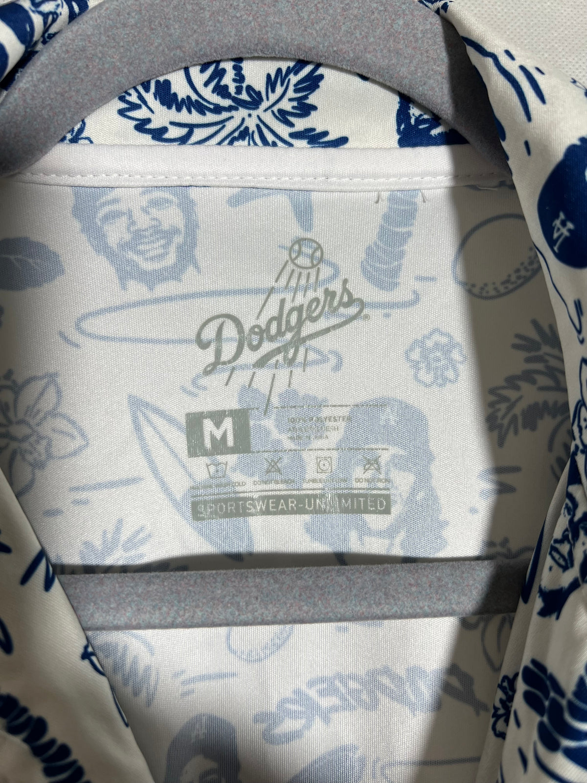 Close-up of the inside collar of a white and blue patterned shirt on a hanger, featuring a Dodgers logo and a size M label.