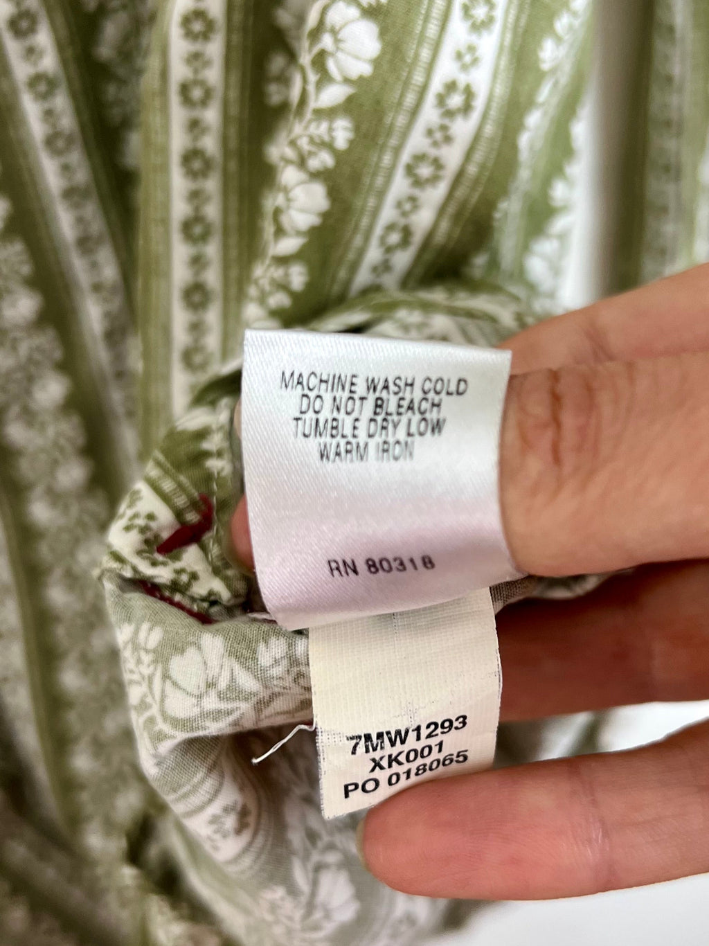 A close-up of a hand holding a white care label against a green and white patterned garment fabric.
