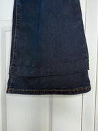 A close-up of a dark blue denim garment, likely a skirt or pants leg, hanging against a white paneled door. The fabric shows dark blue wash details, visible stitching, and a folded hem.