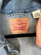 Close-up of a denim jacket's inner neck label showing the classic tan leather Levi's Strauss & Co. patch, with a hand holding a country-of-origin tag next to it.