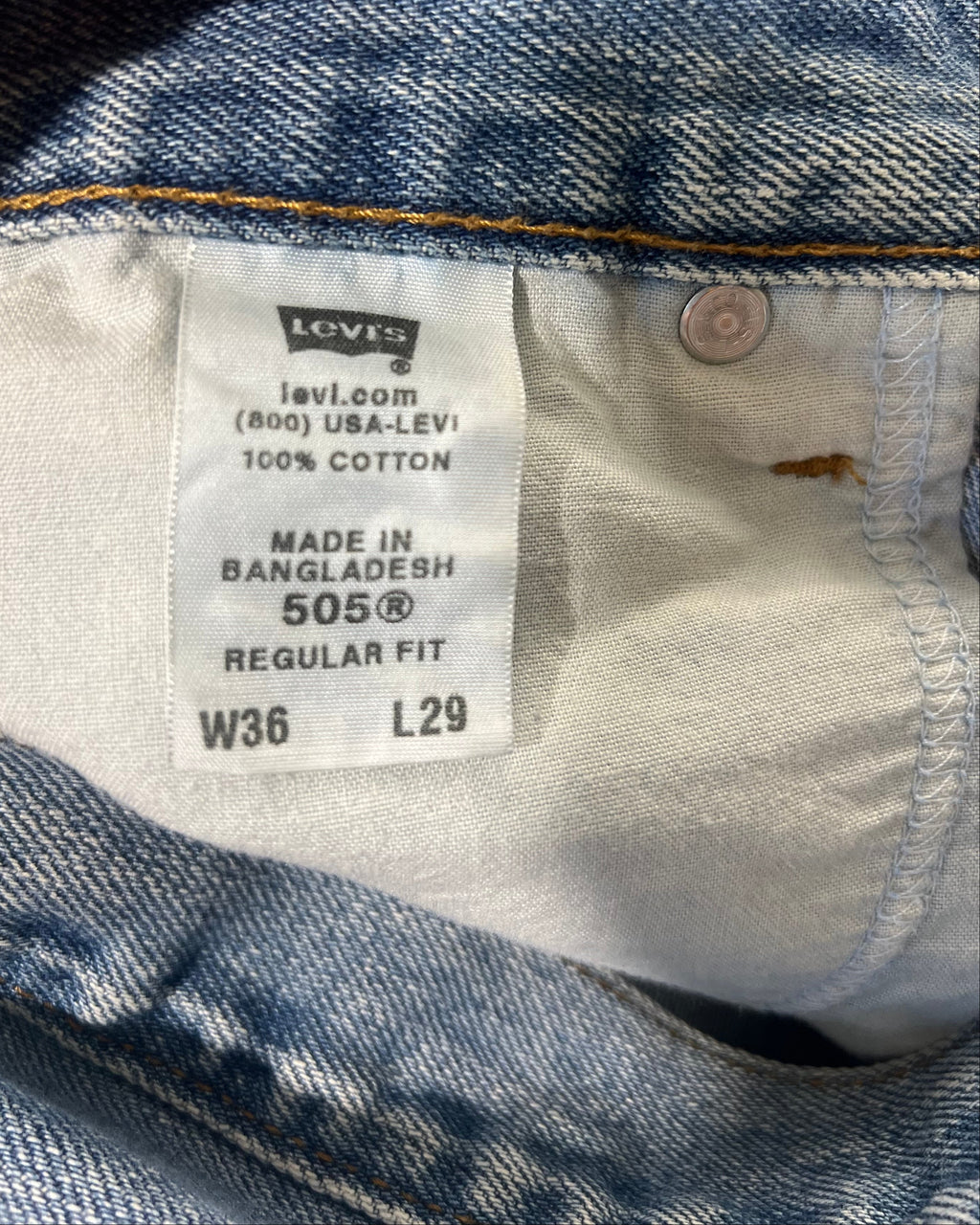Close-up of a Levi's denim garment interior showing the size and care label, with a finger holding the hem open.