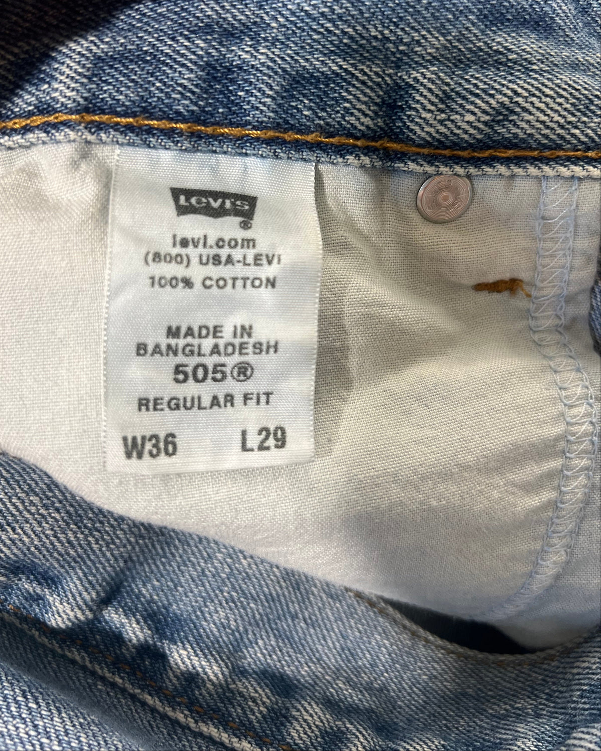 Close-up of a Levi's denim garment interior showing the size and care label, with a finger holding the hem open.