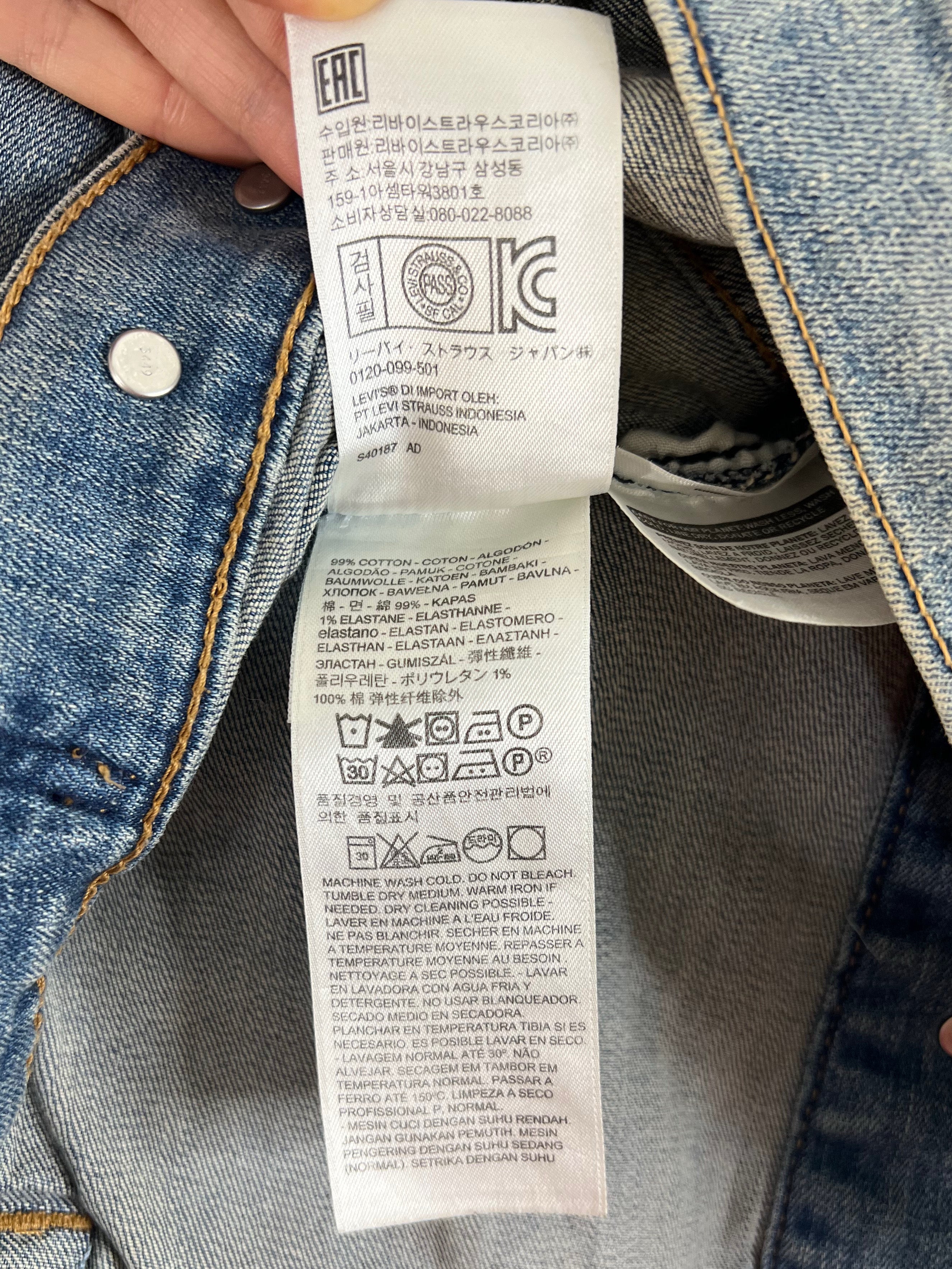 Close-up of a denim jacket's inner label held by a hand, showing the brand 'EBC' and care instructions on a blue denim background.