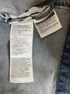 Close-up of the inside waistband of light blue denim jeans showing two white sewn-in care labels with printed garment care instructions in Spanish and English.