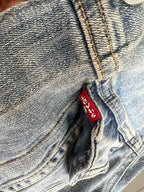 Close-up of a pair of light-wash blue denim jeans showing the iconic red Levi's waistband label and detailed stitching.