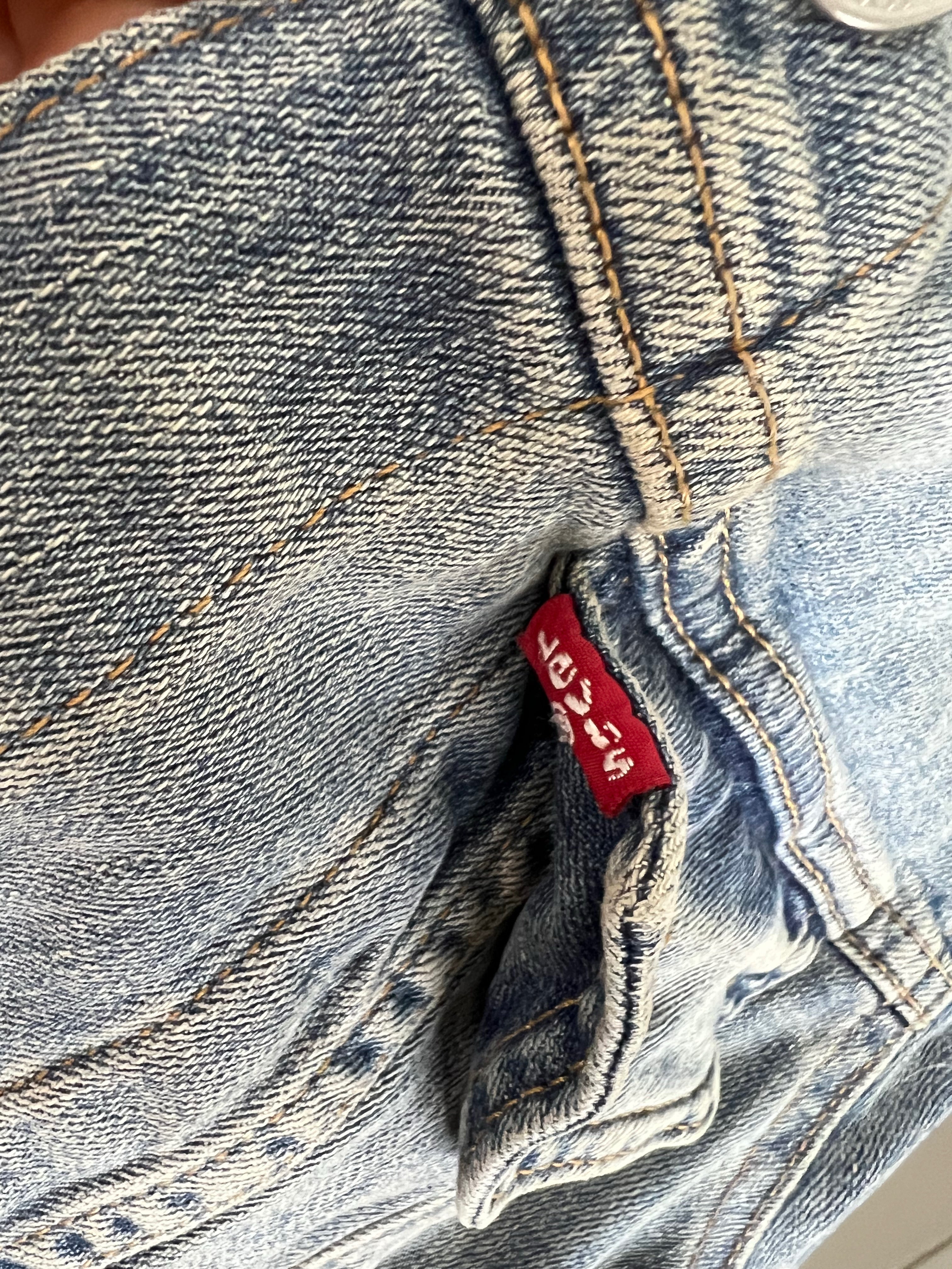 Close-up of a pair of light-wash blue denim jeans showing the iconic red Levi's waistband label and detailed stitching.