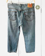 Back view of light blue Levi's denim jeans hanging on a wooden hanger against a white paneled background, showing the classic red tab and leather patch on the waistband.