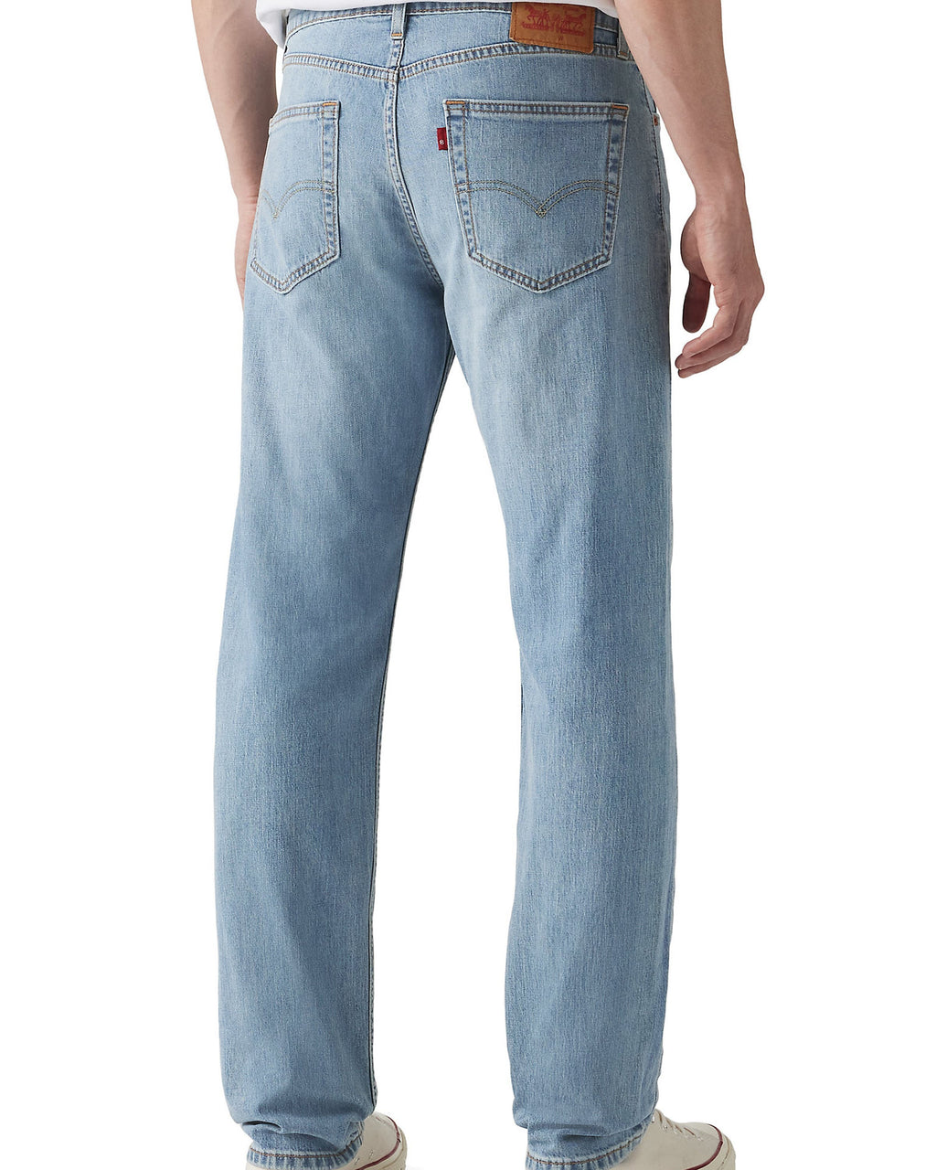 Rear view of a person wearing light-wash blue denim jeans with a white t-shirt and white low-top sneakers, shown against a plain white studio background.