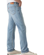 A person shown from the waist down wearing light-wash blue jeans, a white t-shirt, and white low-top sneakers against a plain white studio background.