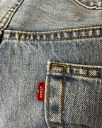 Close-up of a light blue denim garment, showing the back pocket with orange contrast stitching and a red Levi's waist tab.