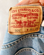 A close-up of a person's hand holding a pair of blue denim jeans to show the iconic tan leather Levi's waistband label.