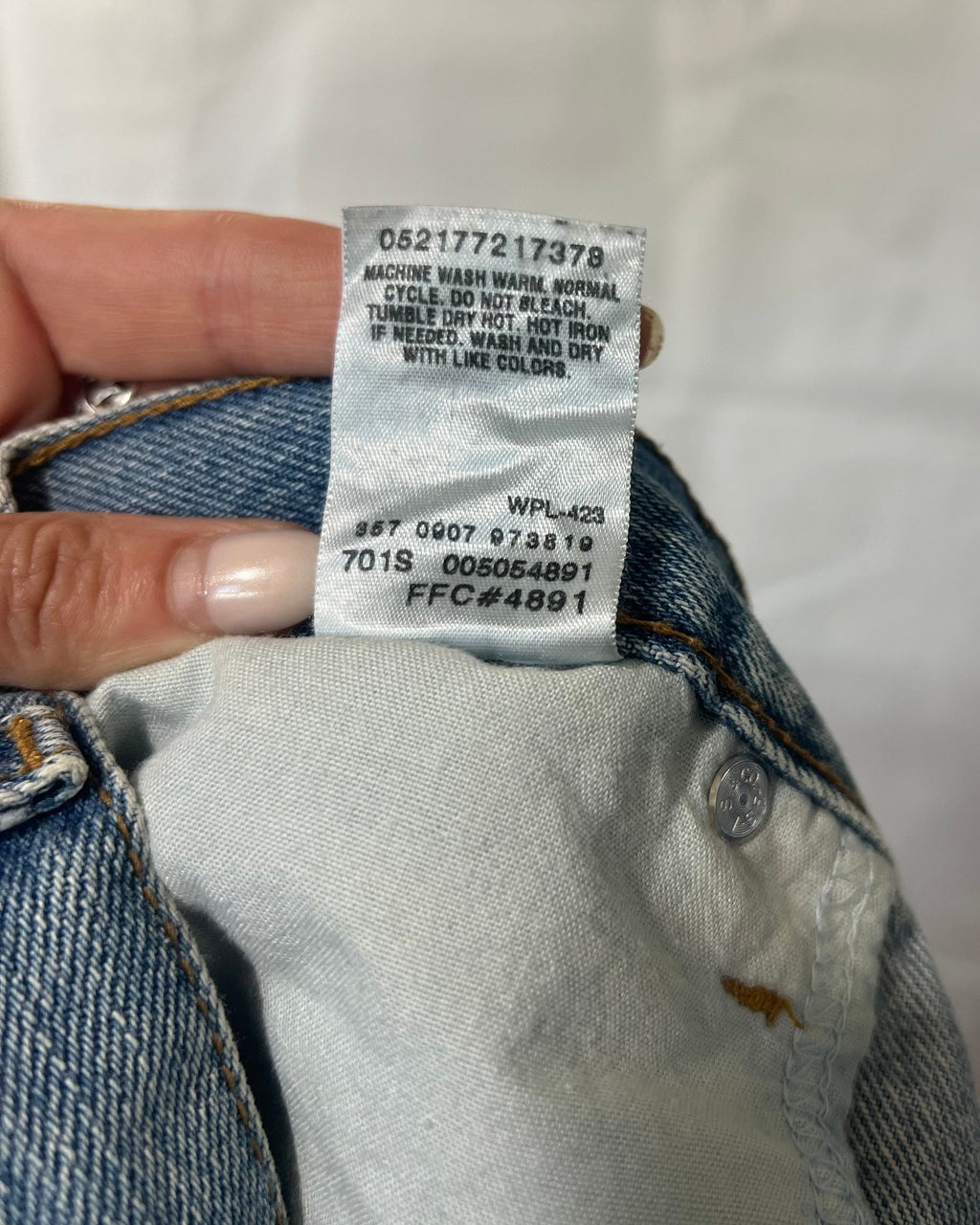 A close-up of a hand holding the inside waistband of a blue denim jacket to show the size and care label.