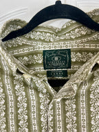 A close-up of a collared button-up shirt hanging on a black hanger, featuring an olive green and cream floral pattern. The neck label clearly shows the brand 'Sucky Brand' and 'Dunlap's America'.
