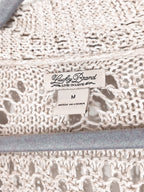 Close-up of a cream-colored crochet knit fabric with a visible sewn-in label reading 'Lucky Brand' and size 'M'.