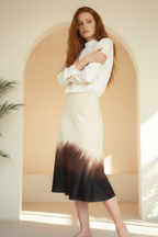 Woman wearing a white blouse and a black and white gradient skirt in a bright room.