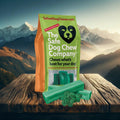 Green package of 'The Safe Dog Chew Company' with two green dog chews on a wooden surface with mountain background.