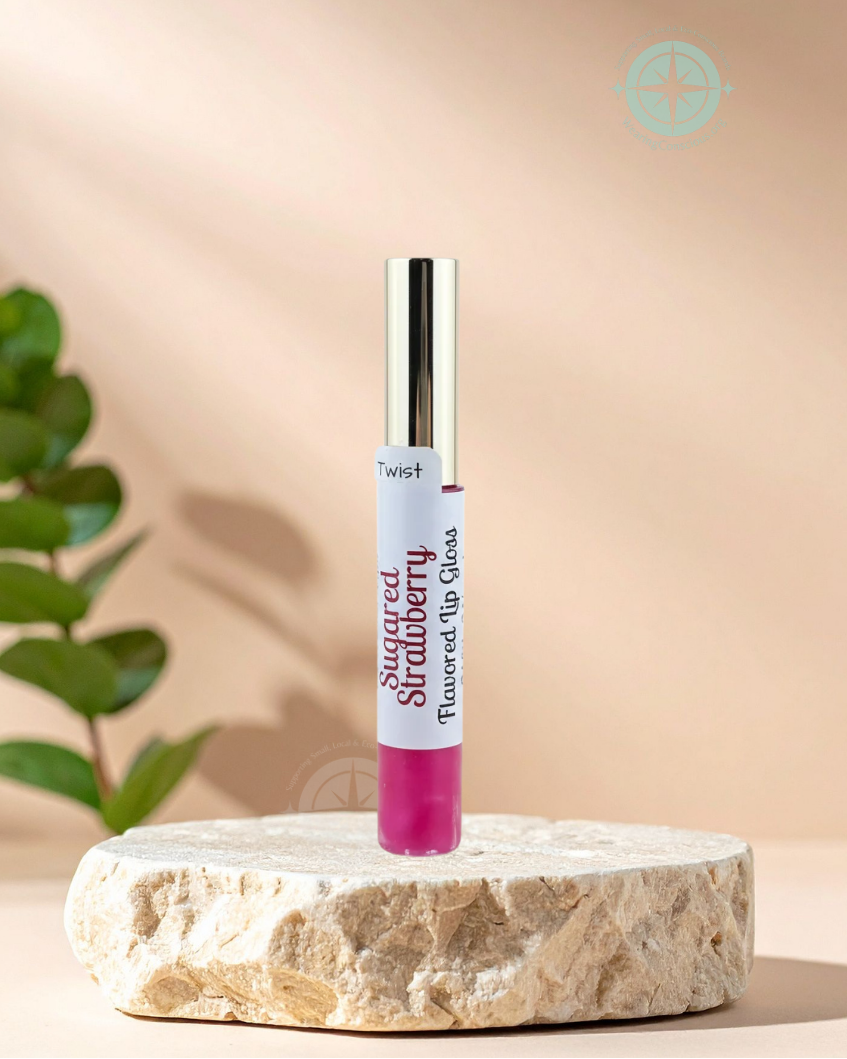 A tube of Flavored Lip Gloss in Sugared Strawberry is displayed on a round stone pedestal. The lip gloss tube is white with a silver cap and features a bright pink gloss visible at the bottom.