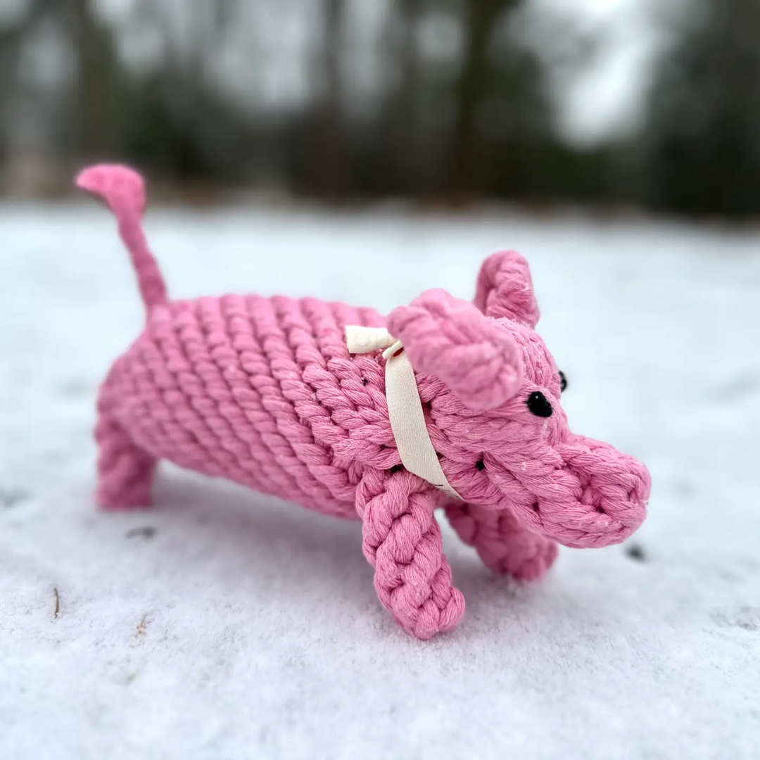 Pink knitted dog toy on a snowy ground with blurred natural background