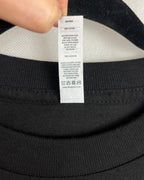 Close-up of a black crewneck t-shirt showing the inner neck label, held by a hand at the top edge.