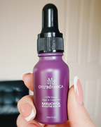 A hand holding a small purple dropper bottle of Oyu Botanica Bakuchiol Booster Serum against a blurred indoor background.