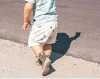 Child walking on a road wearing light-colored pants and brown shoes.