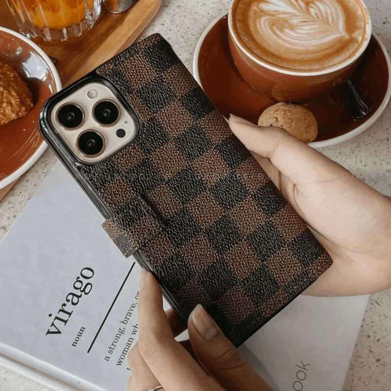 Person holding a phone with a checkered case next to a cappuccino and beer on a table.