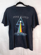 A vintage black Pink Floyd 'The Dark Side of the Moon' graphic t-shirt hanging on a black hanger against a light gray fabric backdrop. The shirt features the band's name in white text above the iconic prism graphic with a rainbow beam of light.