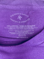 Close-up of a purple t-shirt collar showing the inner label with 'The Prince Estate Official & Approved' branding and cotton manufacturing details.