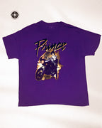 A purple short-sleeve t-shirt featuring a graphic print of the band Prince riding a motorcycle with the word 'Prince' written in a stylized font across the chest.