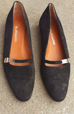 Pair of black suede shoes with metallic straps on a textured surface