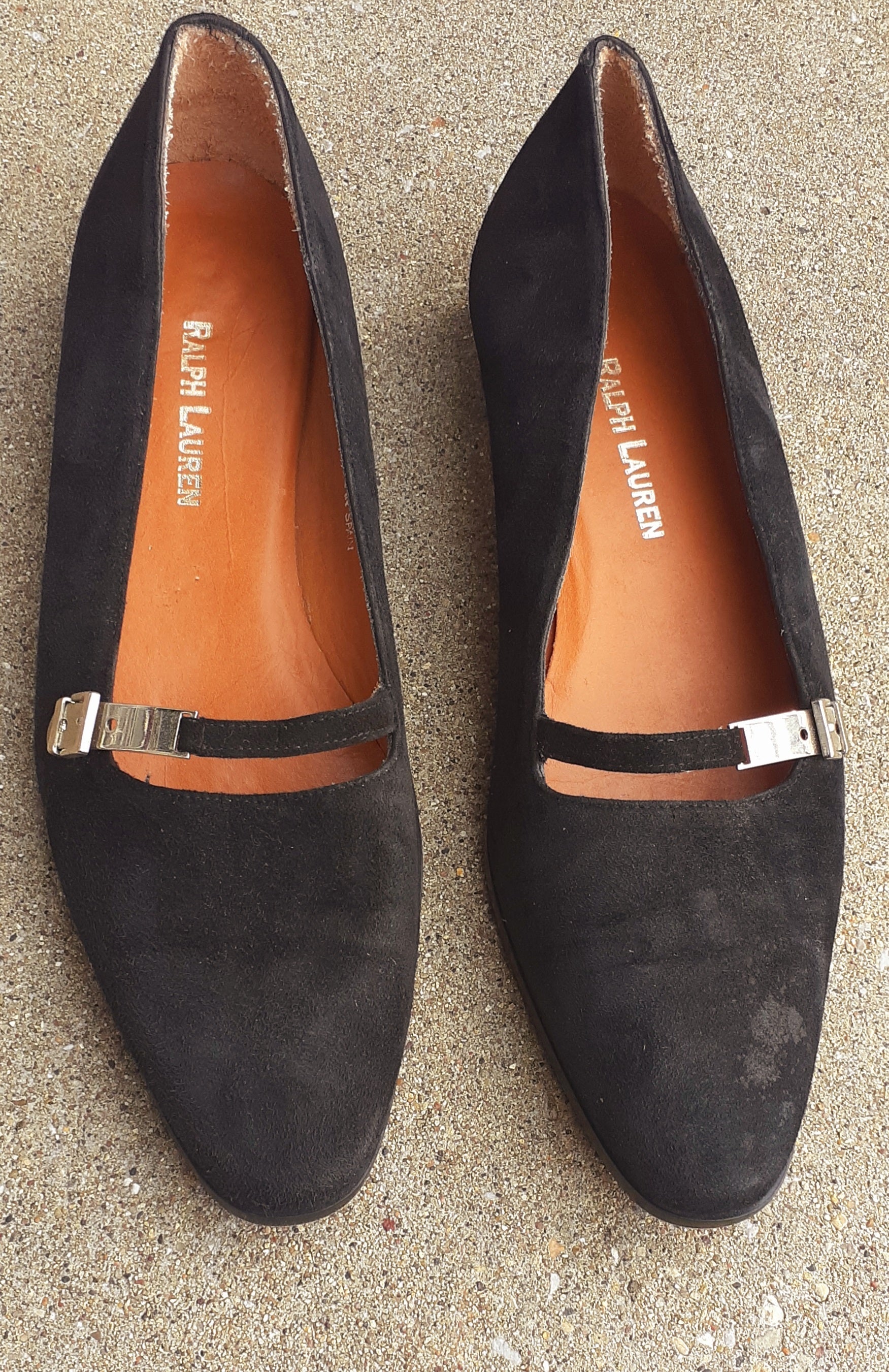 Pair of black suede shoes with metallic straps on a textured surface