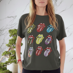 A woman with glasses and long blonde hair stands in front of a white marble wall, wearing a dark gray graphic t-shirt featuring the Rolling Stones 'Love Rock Roll' tongue and lips logo design.