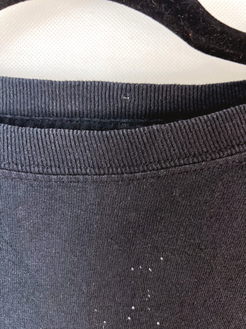 Close-up of a dark charcoal gray ribbed knit garment, showing the collar and upper chest area with a few small white lint or dust specks visible on the fabric.