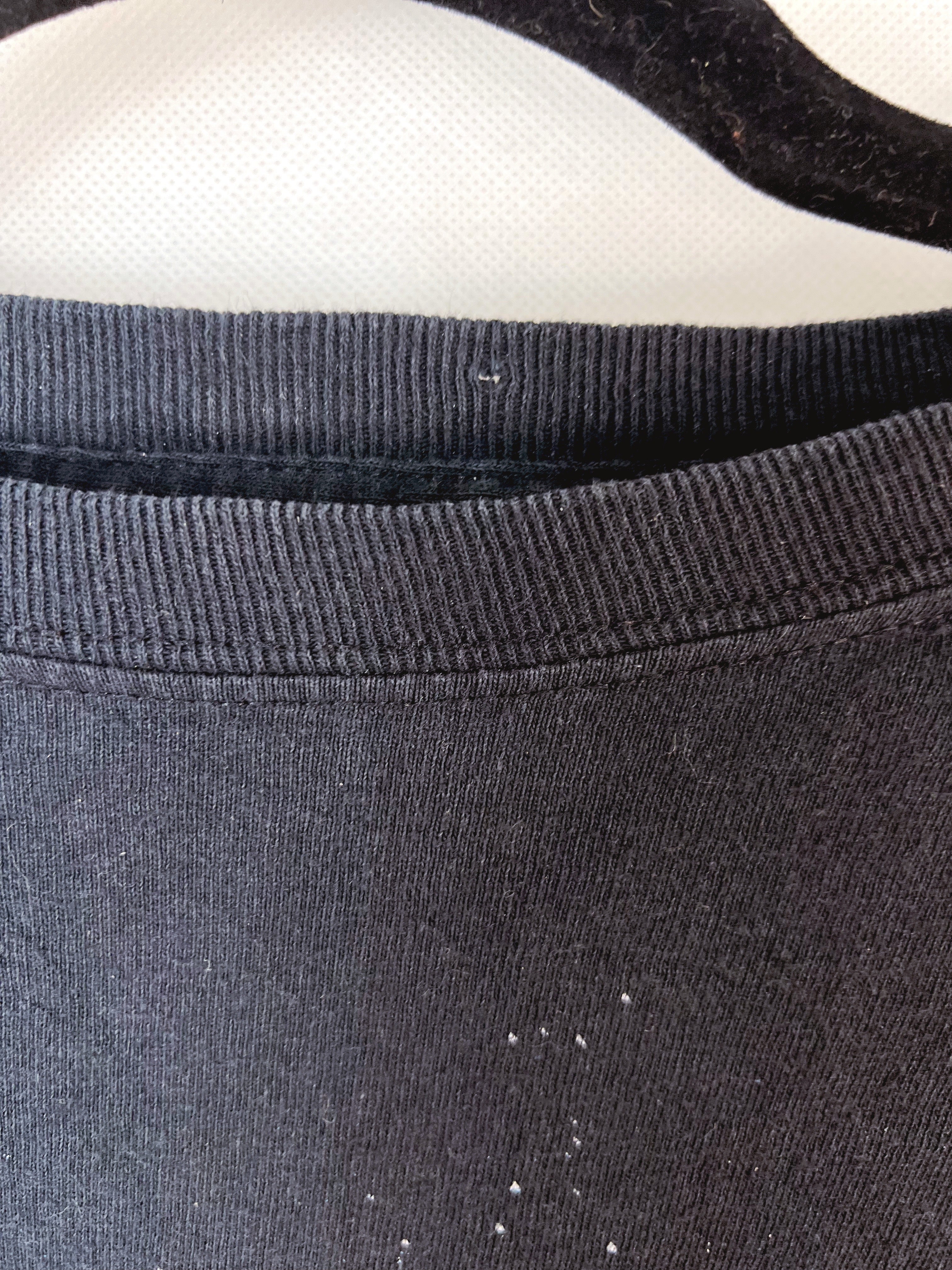 Close-up of a dark charcoal gray ribbed knit garment, showing the collar and upper chest area with a few small white lint or dust specks visible on the fabric.
